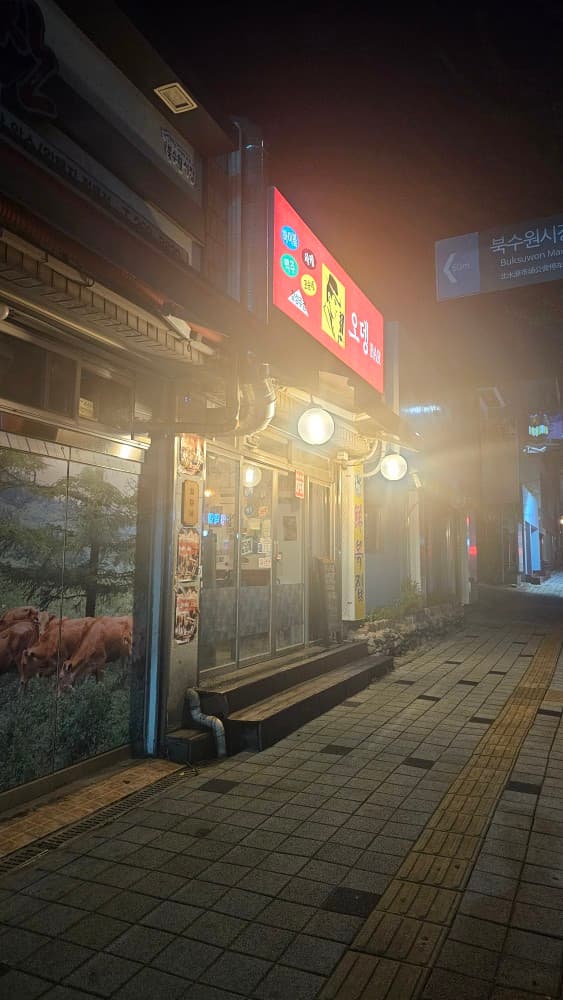 수원 꼬순네 오뎅바의 따뜻한 야간 외경. 붉은색 간판과 은은한 조명이 어우러져 퇴근 후 혼술하기 좋은 아늑한 가게 입구 모습.