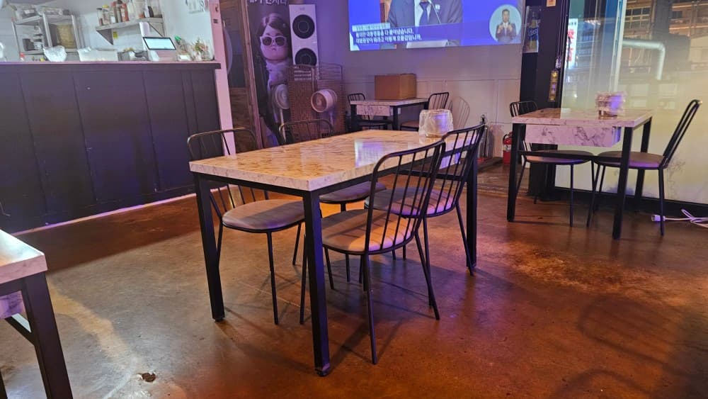 민자야 포차의 세련된 대리석 테이블과 TV가 설치된 내부 전경, 혼술하기 좋은 아늑한 분위기