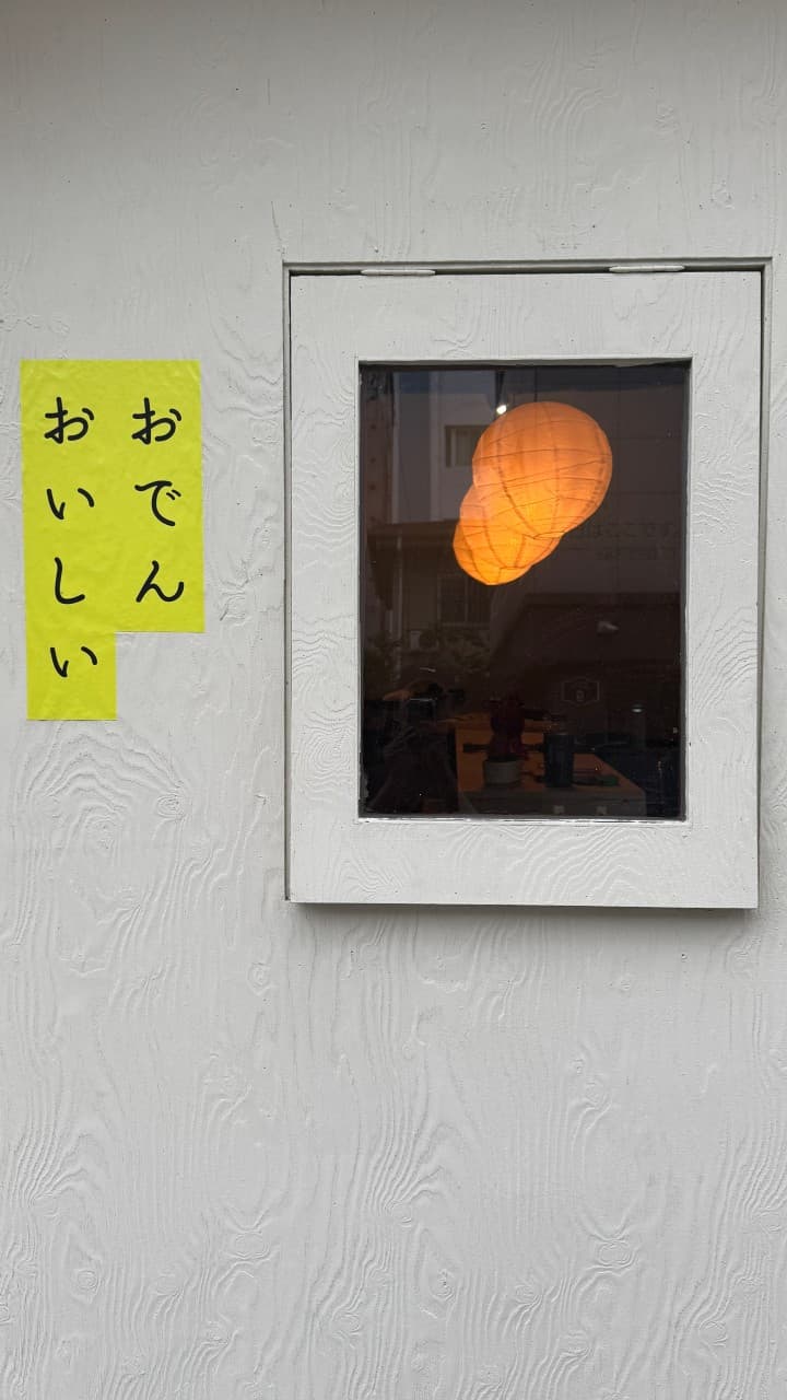 선술집 코코 외벽의 흰 나무 질감과 일본어 문구, 창문 너머 주황색 전등이 빛나는 아늑한 혼술 공간.