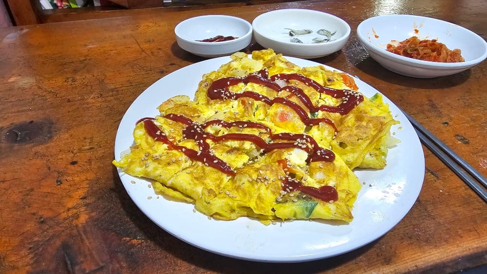 동래 오딧세이 포차, 케첩을 뿌린 두툼한 계란말이와 정갈한 밑반찬. 나무 테이블 위 아늑한 분위기로 혼술하기 좋은 안주.