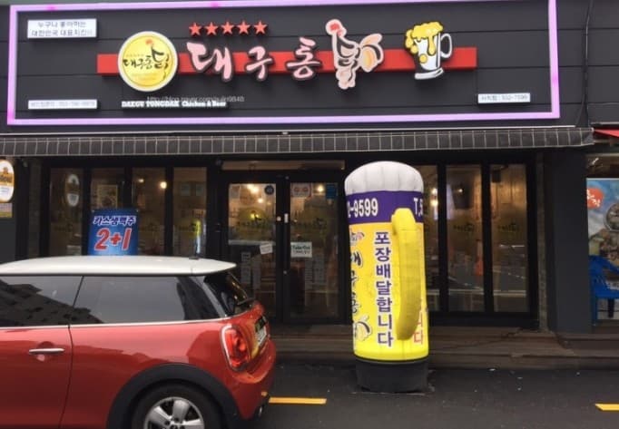 맥주잔 형태의 대형 풍선과 통유리 출입문이 배치된 건물 외관 앞 붉은색 소형 승용차