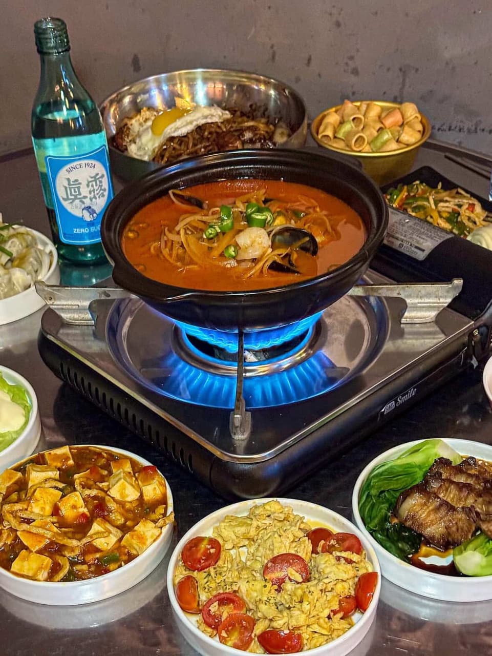 부산 부엉이포차(가야대로747번길 69)의 푸짐한 상차림. 가스레인지 위 끓는 얼큰한 탕과 마파두부, 동파육 등 다채로운 메뉴가 있어 혼술이나 혼밥하기 좋습니다. 소주 한 잔 곁들이기 좋은 다양한 포차 안주들이 테이블을 가득 채운 모습입니다.