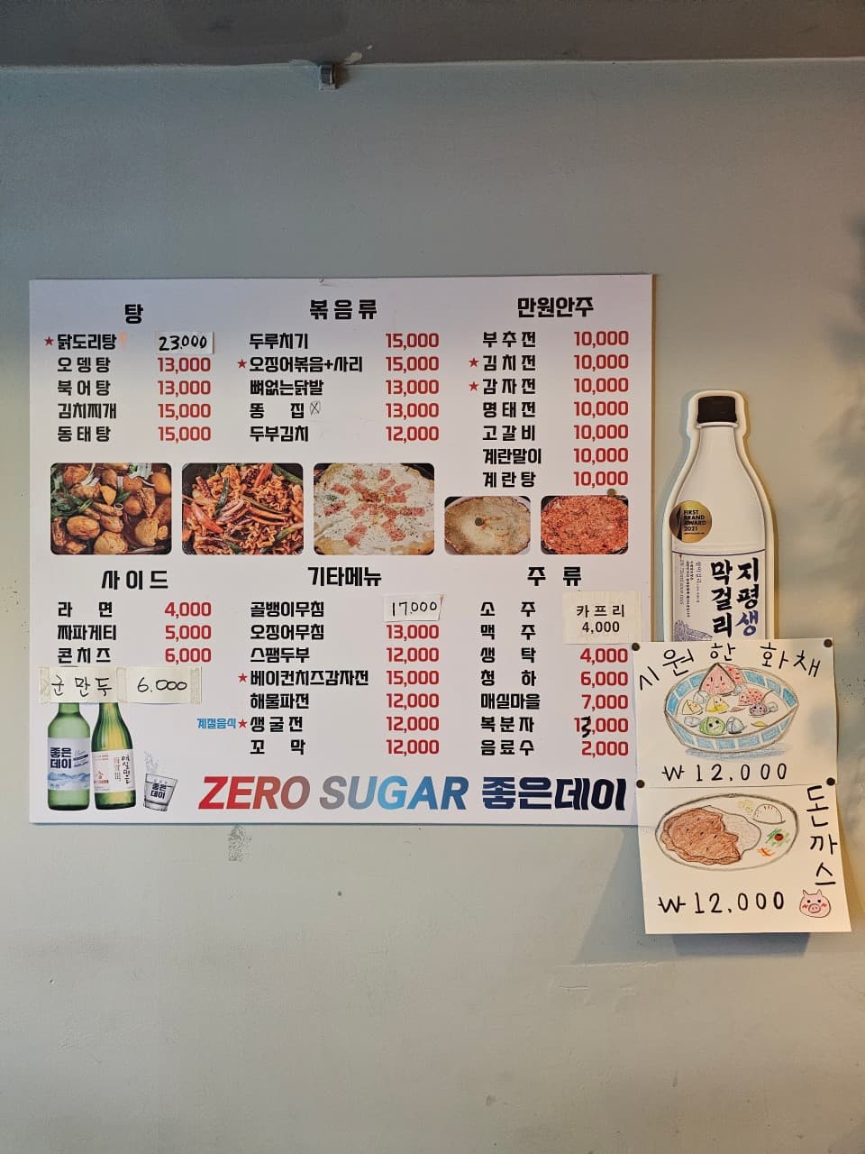 만원 안주와 다양한 요리가 사진과 함께 기재된 벽면 메뉴판, 옆면에 부착된 수필 안주 안내문