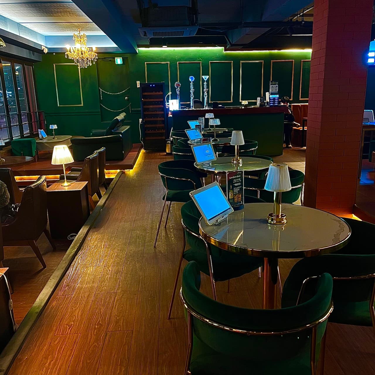초록색 벽면과 목재 바닥, 테이블마다 태블릿과 개인용 스탠드 조명이 배치된 원형 테이블 위주의 좌석 전경