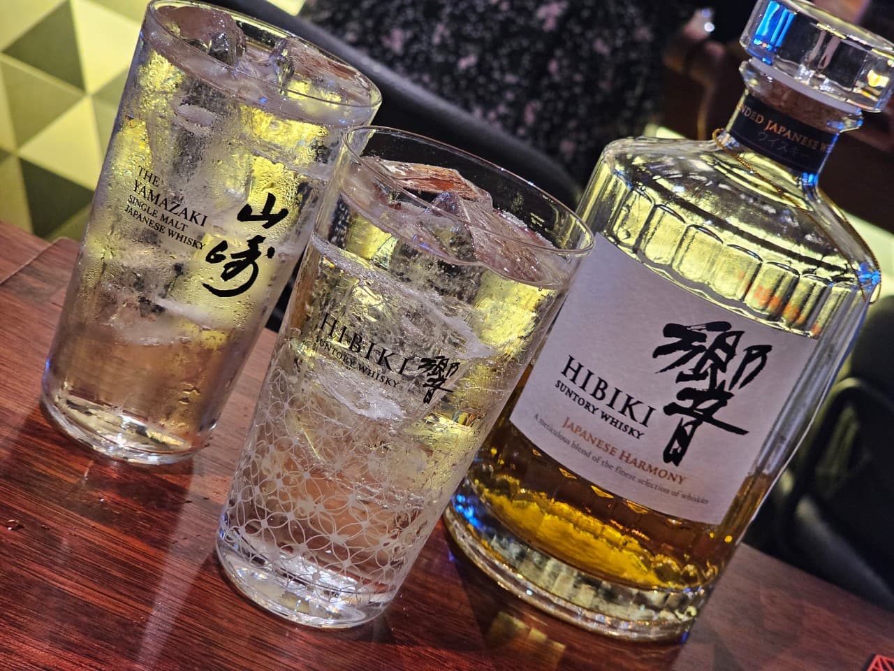 어두운 조명 아래 목재 카운터 위 얼음 가득한 하이볼 잔들과 나란히 놓인 히비키 위스키 병