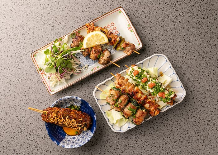 회색 석재 테이블 위 레몬이 올라간 닭꼬치와 양배추를 곁들인 꼬치구이, 계란 노른자가 담긴 1인용 안주 구성