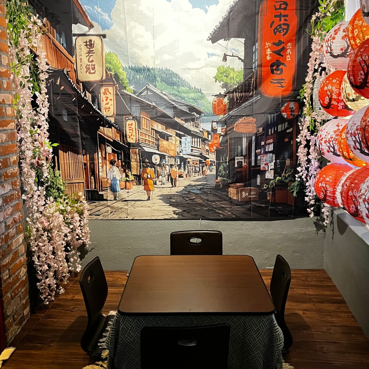 일본 거리 풍경 포스터와 붉은 등이 장식된 벽면 아래 코타츠 테이블과 1인용 좌식 의자가 배치된 공간