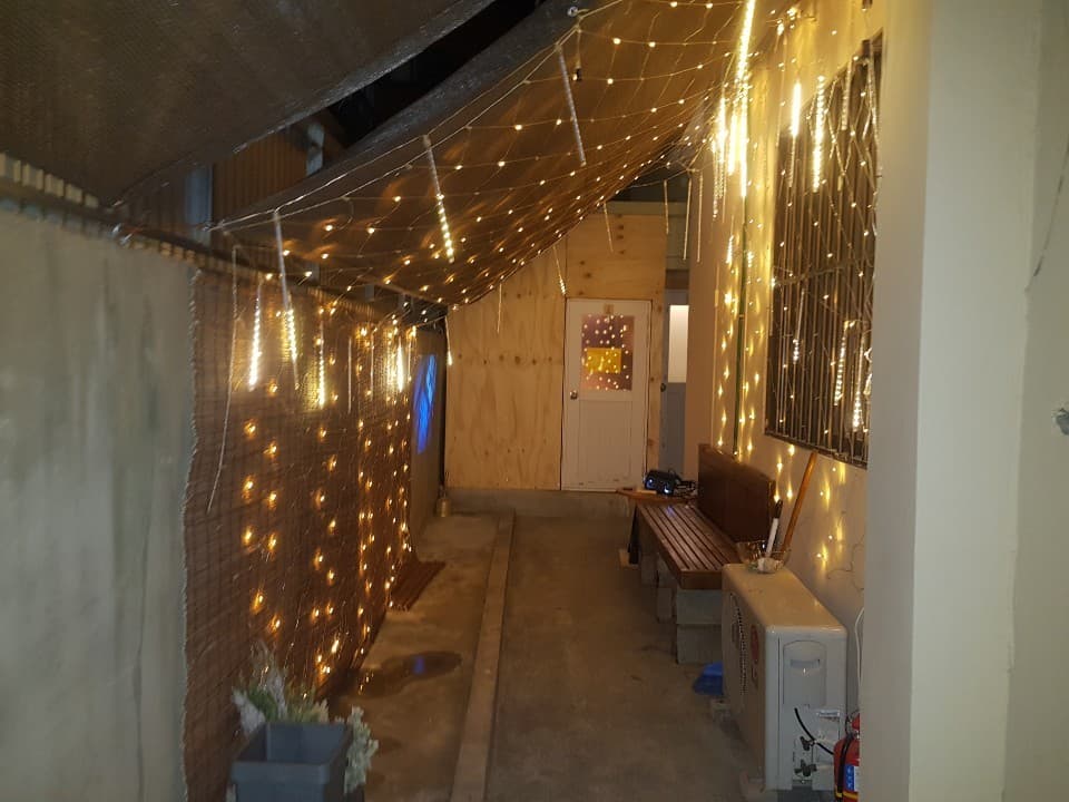 노란 전구 조명이 설치된 갈색 천막 아래 좁은 통로와 벽면에 배치된 대기용 나무 벤치 전경