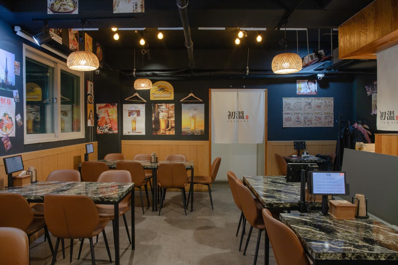 바구니 모양 전등 아래 대리석 무늬 테이블과 갈색 의자, 벽면 포스터와 좌석마다 설치된 주문 전용 태블릿