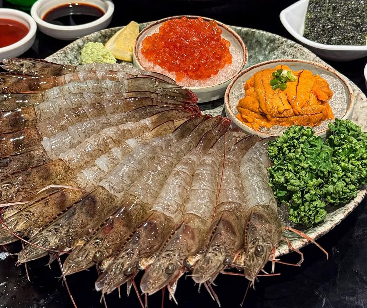 접시에 부채꼴로 펼쳐진 생새우 회와 얼음 위 연어알, 성게알 종지. 와사비와 김, 소스가 곁들여진 1인용 구성의 해산물 플레이트