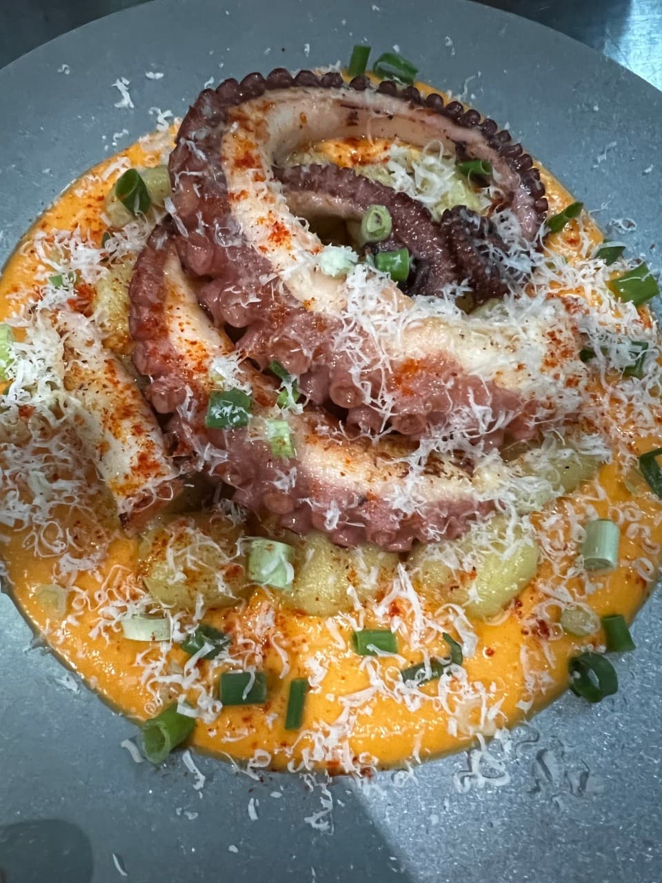 주황색 소스 위 노릇하게 구워진 문어 다리와 알감자 위로 잘게 갈린 치즈가 뿌려진 접시