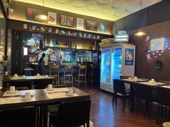 노란 조명 아래 1인용 바 테이블과 높은 의자, 흰색 식기가 세팅된 짙은 색의 목재 테이블이 배치된 실내 전경