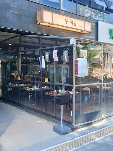 투명 비닐 천막 너머로 보이는 소규모 테이블과 의자, 흰색 제등과 벽면에 진열된 술병들이 배치된 내부 전경