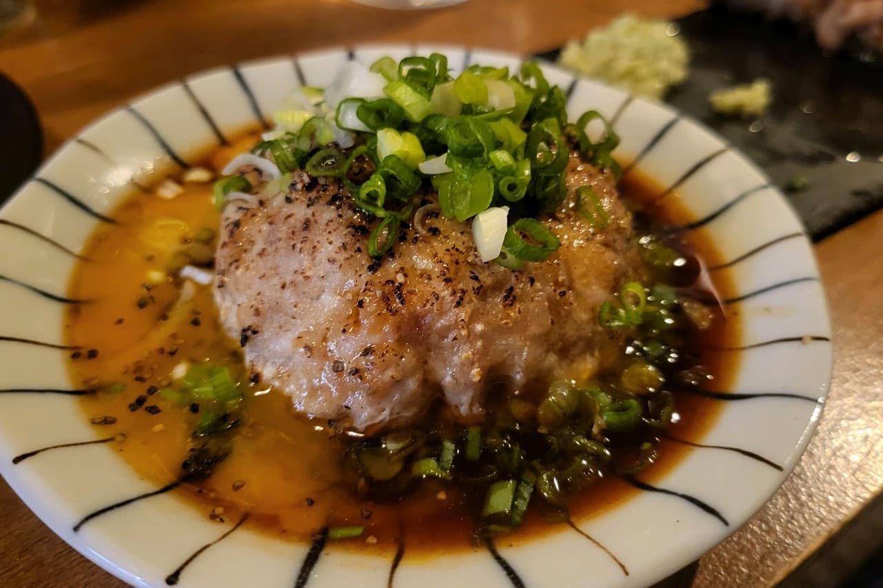 나무 카운터 위 검은 선 무늬 그릇에 담긴 고기 완자와 계란 노른자, 수북하게 쌓인 송송 썬 파