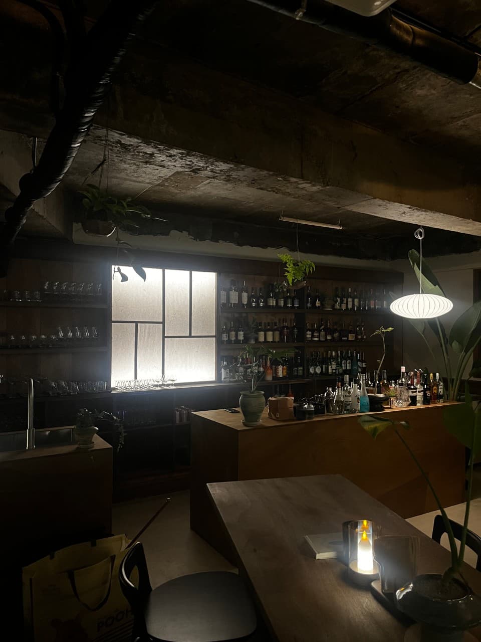 노출 콘크리트 천장 아래 목재 카운터와 술병이 진열된 선반, 테이블 위 촛불 조명과 1인용 좌석