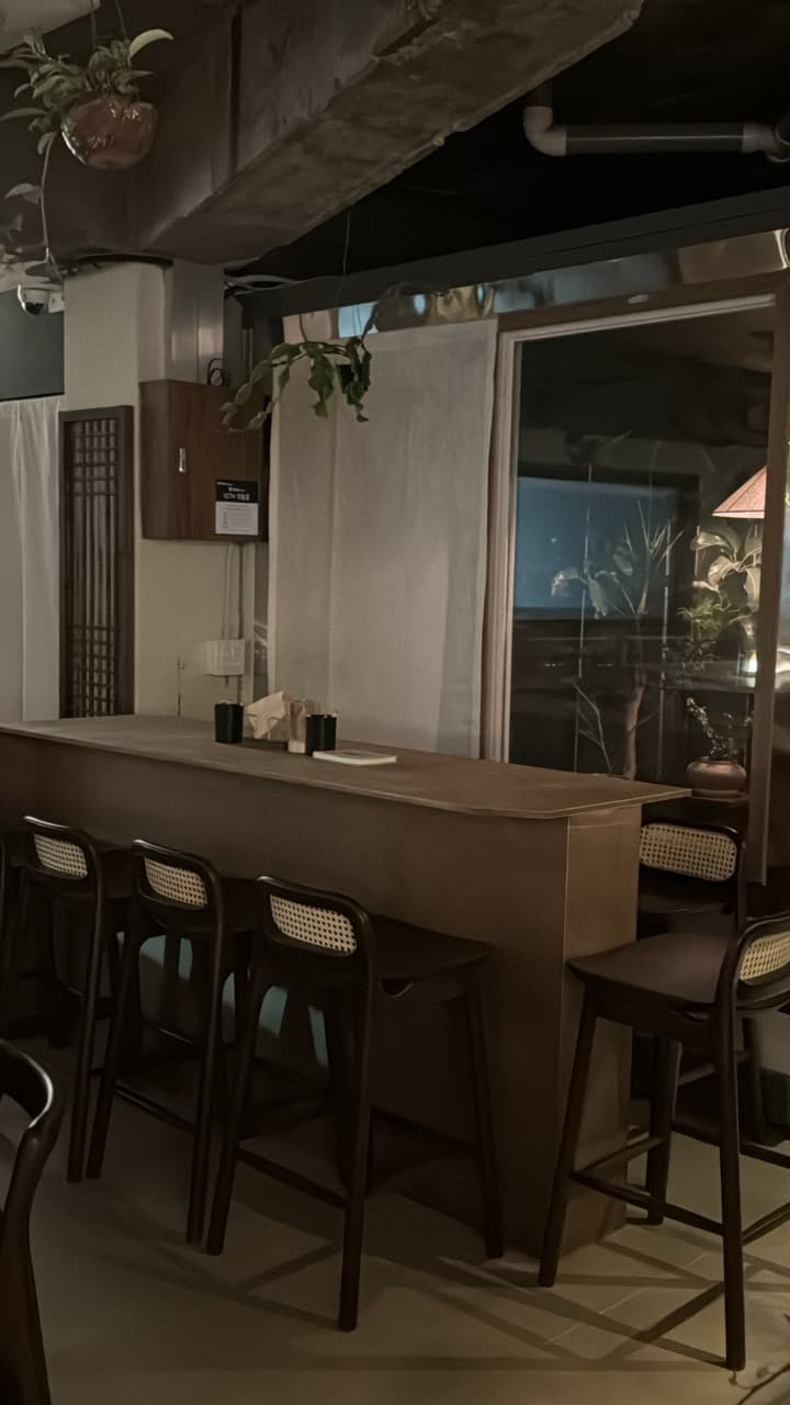 어두운 조명 아래 일렬로 배치된 목재 바 테이블과 라탄 소재 등받이가 있는 높은 의자들