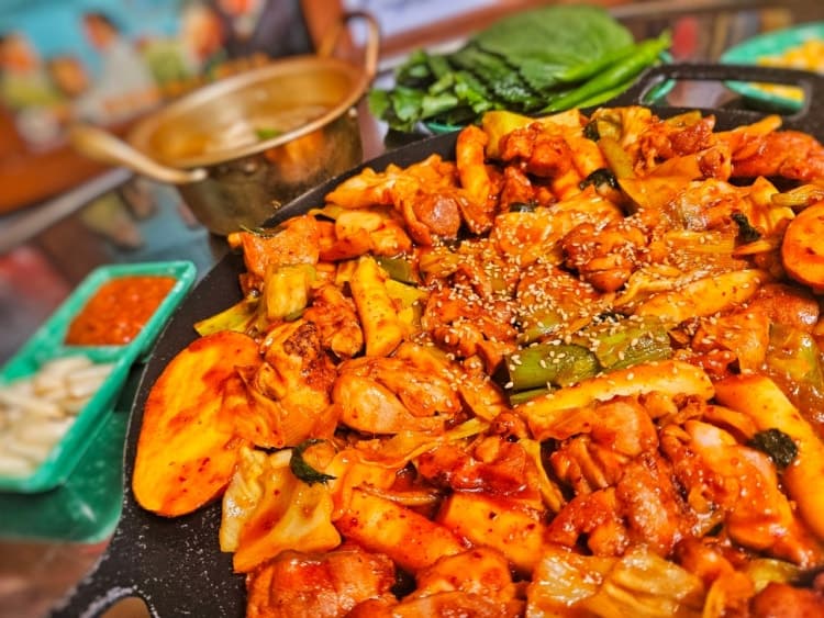 철판 위 붉은 양념의 닭갈비와 떡, 쌈 채소와 소형 양은 냄비가 차려진 1인 식탁 전경