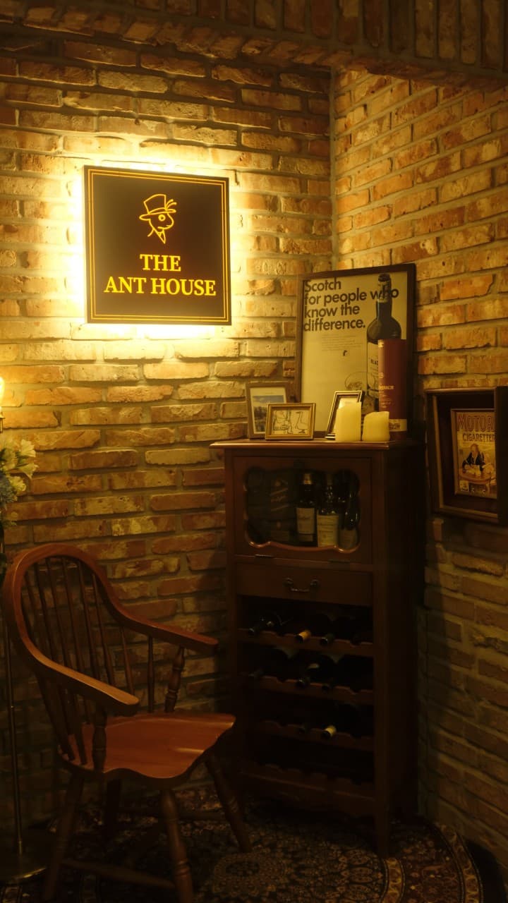 붉은 벽돌 벽면의 노란 조명 간판과 술병이 진열된 목재 수납장, 그 옆에 놓인 1인용 나무 의자