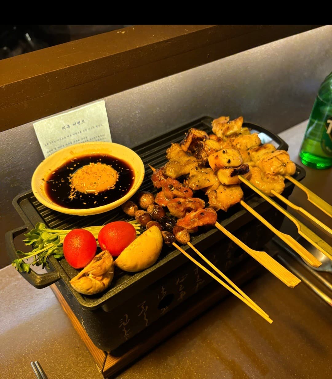 목재 다찌석 위 1인용 미니 화로에 놓인 다양한 닭꼬치와 노른자가 담긴 간장 소스, 방울토마토