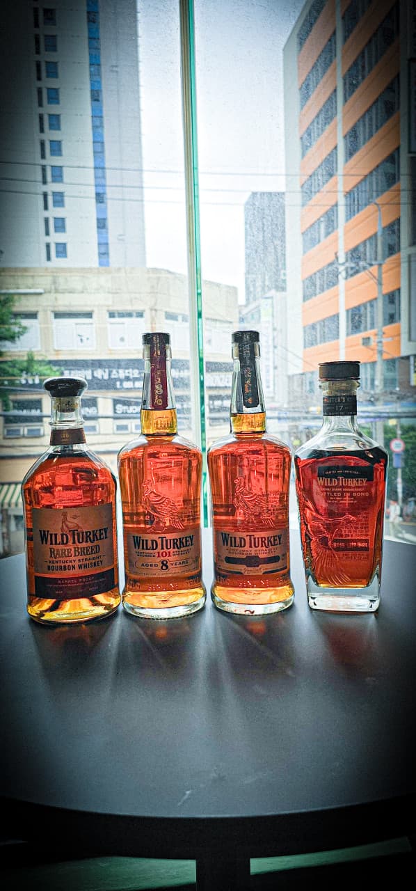 도심 건물이 보이는 창가 쪽 어두운 원형 테이블 위에 일렬로 놓인 네 종류의 위스키 병