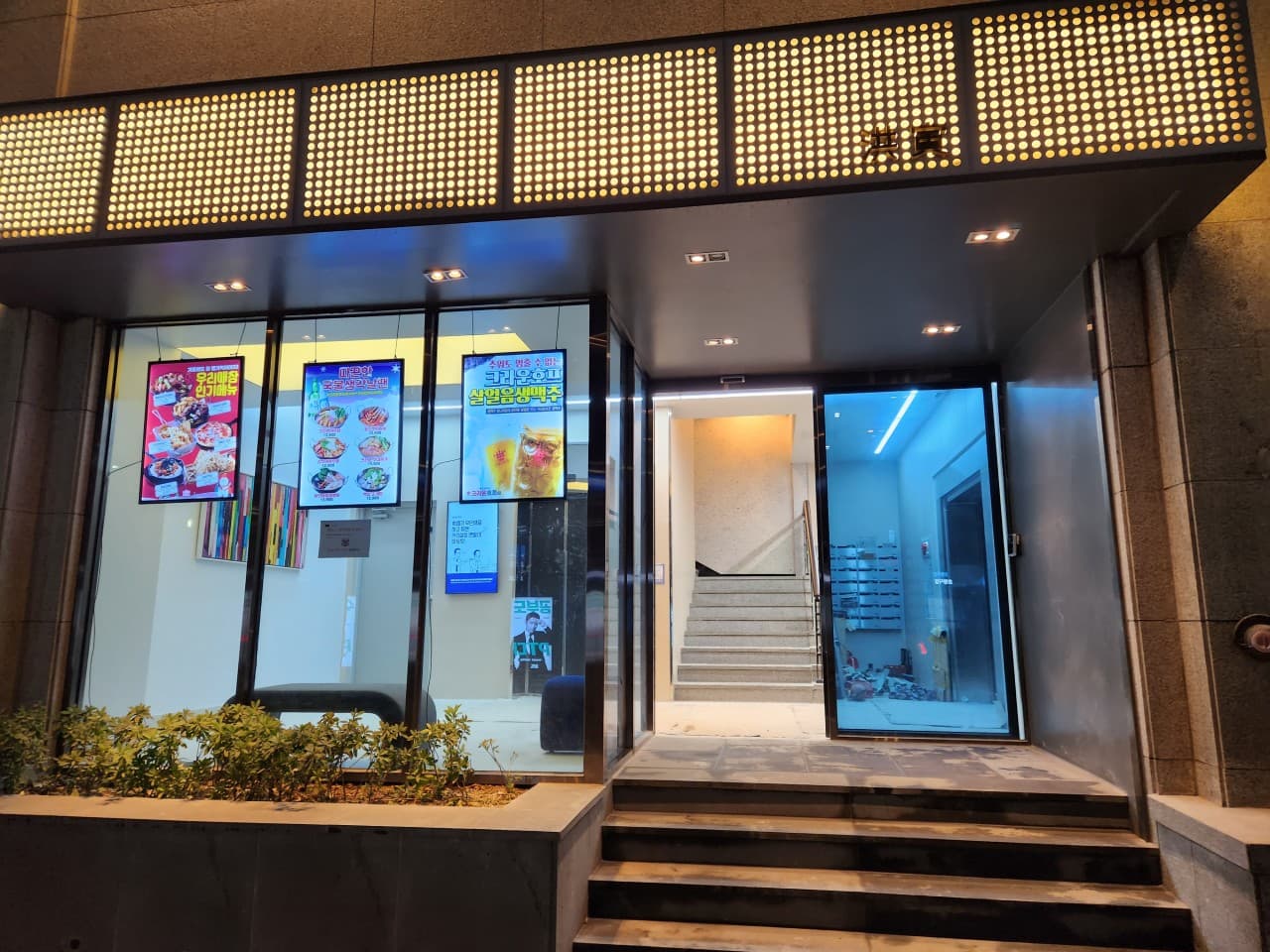 노란 격자형 조명 아래 살얼음 맥주 포스터가 붙은 통유리창과 매장 내부로 이어지는 계단 입구