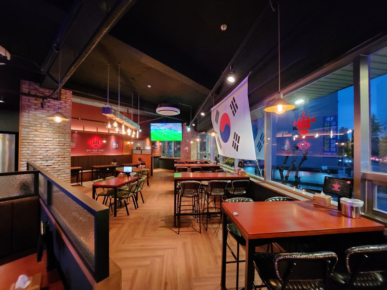 창밖 야경이 보이는 높은 바 테이블과 의자, 황색 조명 아래 배치된 붉은색 목재 테이블과 벽면의 태극기