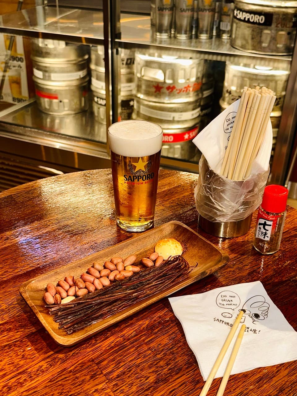 나무 테이블 위 거품이 담긴 생맥주와 땅콩, 마른안주 접시. 젓가락 통과 양념병, 캐릭터 티슈가 놓인 1인용 테이블 구성