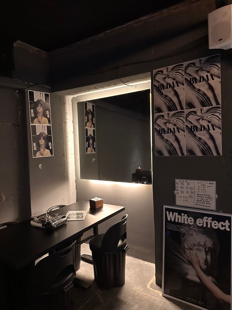 어두운 무채색 벽면과 간접 조명 거울 앞 검은색 테이블, 1인용 좌석 및 휴대용 가스레인지