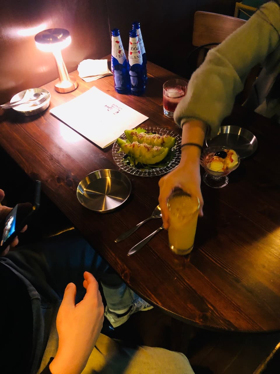 어두운 실내의 목재 테이블 위 은은한 스탠드 조명과 메론 플레이트, 맥주병 및 하이볼 잔