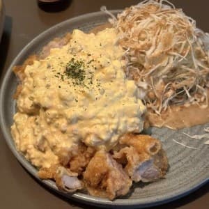 바 테이블 위 회색 원형 접시에 담긴 타르타르 소스 듬뿍 얹은 치킨 난반과 참깨 드레싱 양배추 샐러드