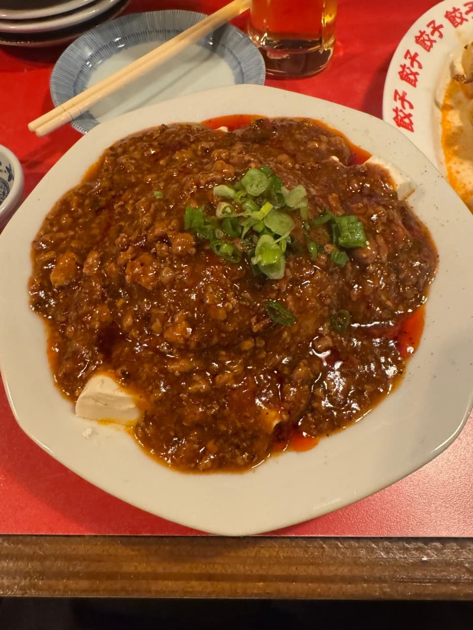 붉은 테이블 위 다진 고기 소스를 얹은 두부 요리와 맥주잔, 나무 젓가락이 놓인 1인 카운터 좌석