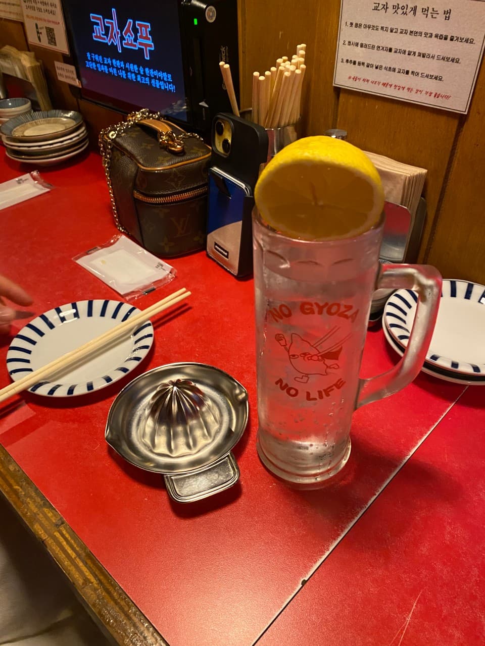 붉은색 카운터 테이블 위 레몬이 얹어진 하이볼 잔과 레몬 스퀴저, 벽면을 마주 보고 놓인 1인용 식기류