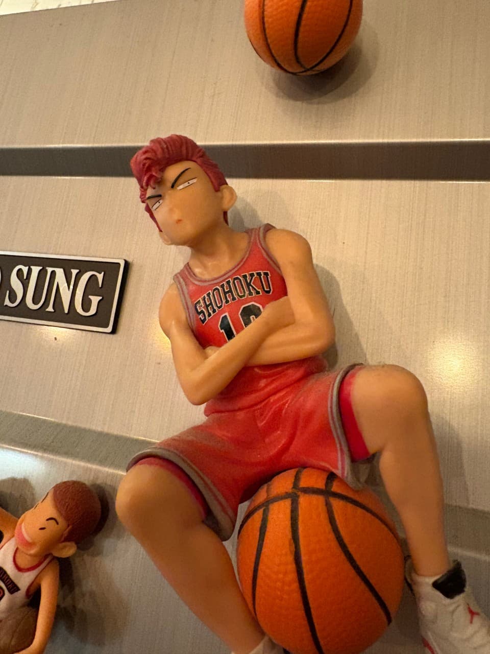 회색 금속 벽면 선반에 놓인 빨간색 유니폼의 농구 선수 피규어와 농구공 모양의 입체적인 장식 소품