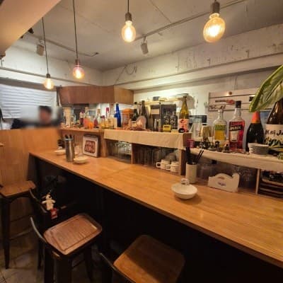 전구색 펜던트 조명 아래 배치된 목재 카운터 테이블과 높은 의자, 선반 위 여러 종류의 술병과 식기류