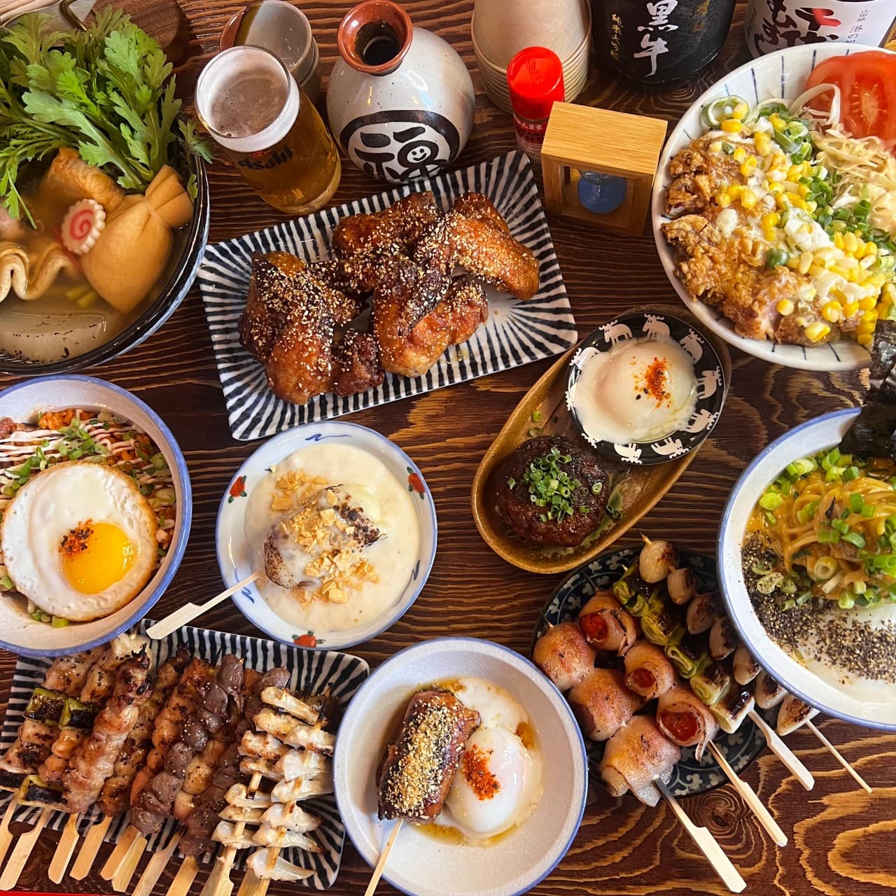 나무 테이블 위 닭꼬치 모듬, 튀긴 날개 요리, 마제소바와 덮밥 등 여러 안주 접시와 생맥주 한 잔