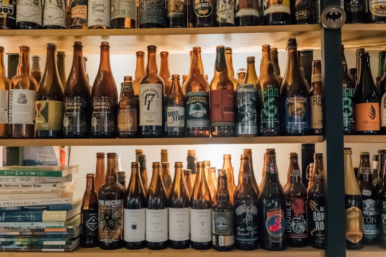 나무 선반마다 빼곡하게 들어찬 다양한 크기의 맥주 병들과 한쪽 구석에 쌓여 있는 서적들