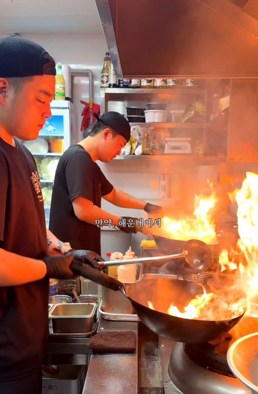 바 테이블 정면의 오픈 주방에서 요리사가 웍을 사용하여 강한 불꽃을 일으키며 요리하는 전경