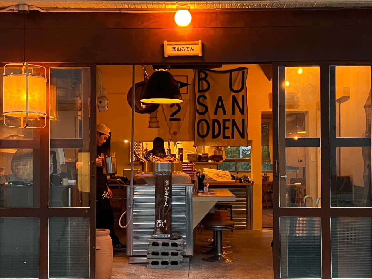 주황색 조명 아래 1인용 의자가 배치된 긴 카운터 좌석과 오뎅 솥이 보이는 매장 내부 전경