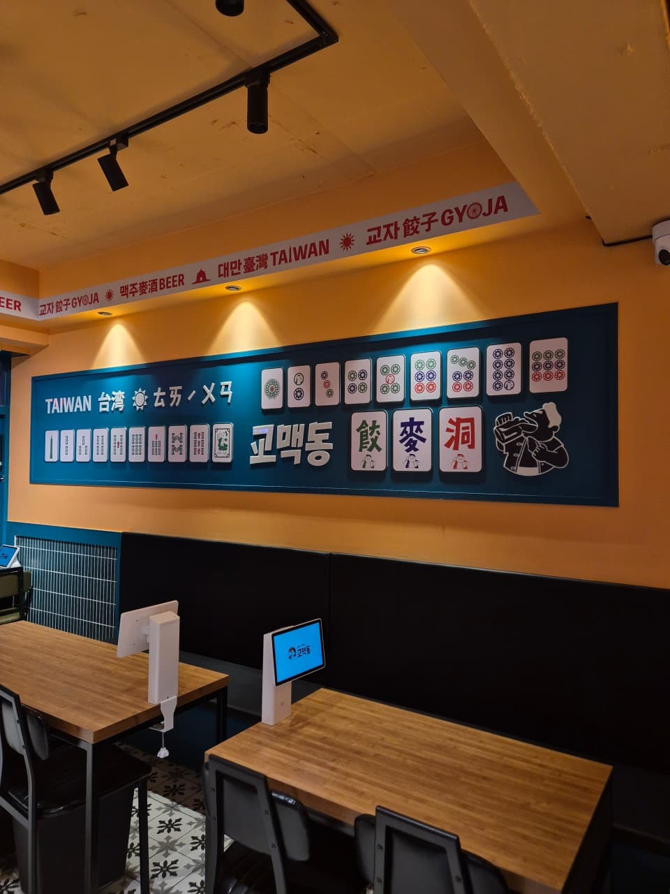 마작 패 디자인의 벽면 장식 아래 태블릿 주문 기기가 설치된 소규모 목재 테이블과 좌석 전경