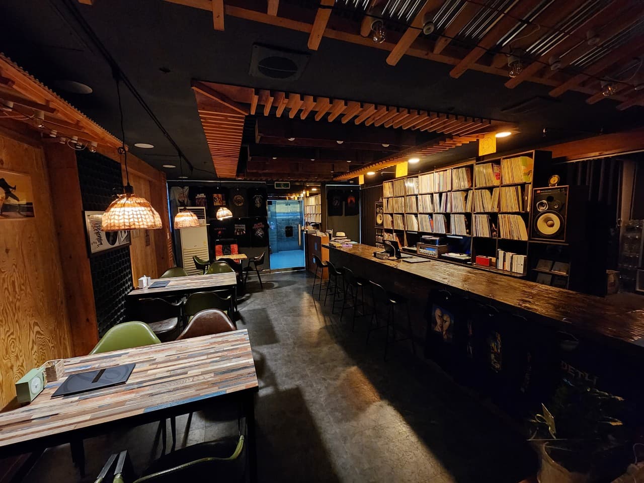 수많은 LP가 진열된 벽면 선반과 긴 나무 바 테이블을 따라 1인용 의자가 배치된 어두운 조명의 실내