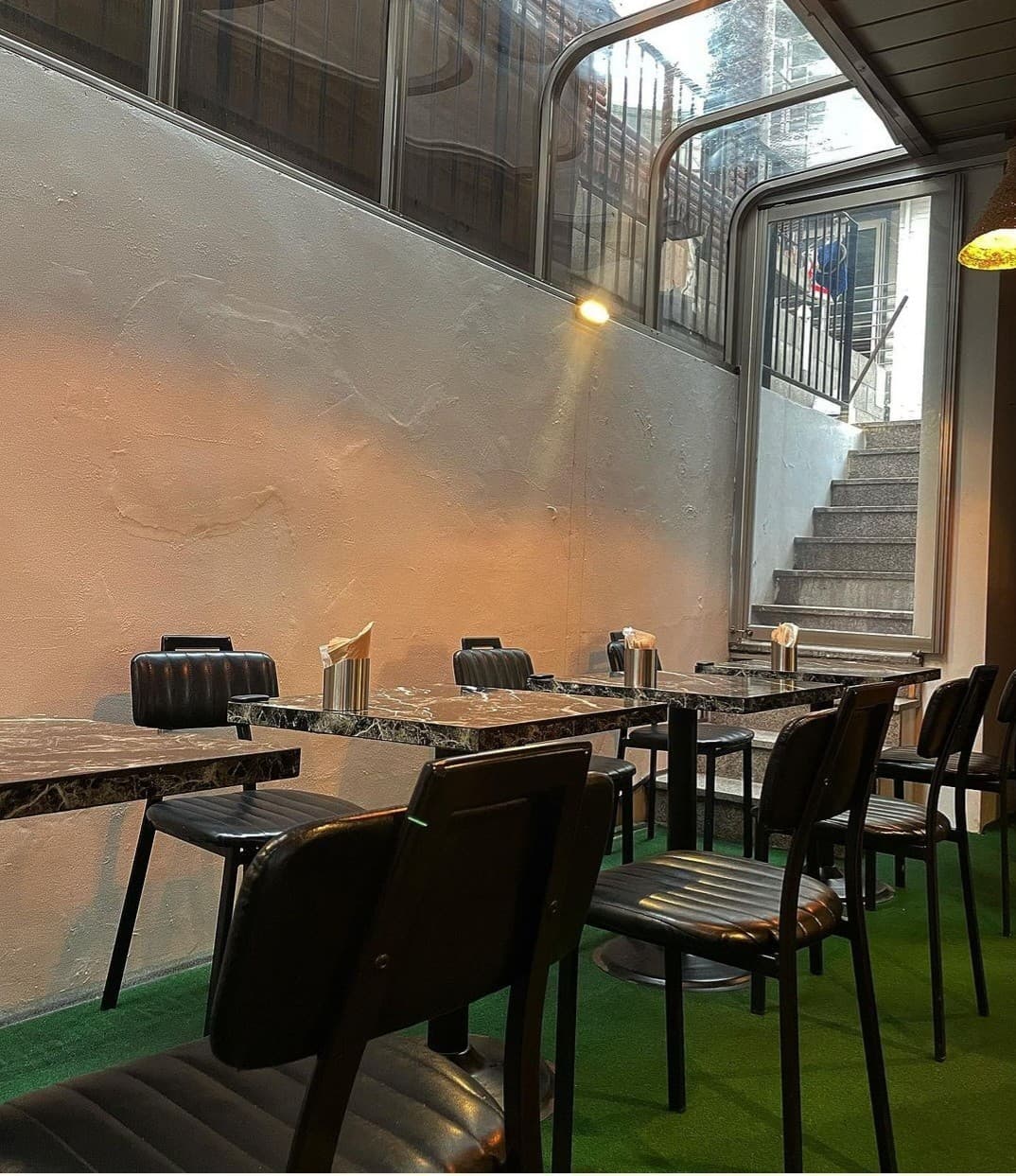 황색 조명이 비치는 벽면을 따라 놓인 대리석 무늬 테이블과 1인용 검정 가죽 의자 및 인조 잔디 바닥