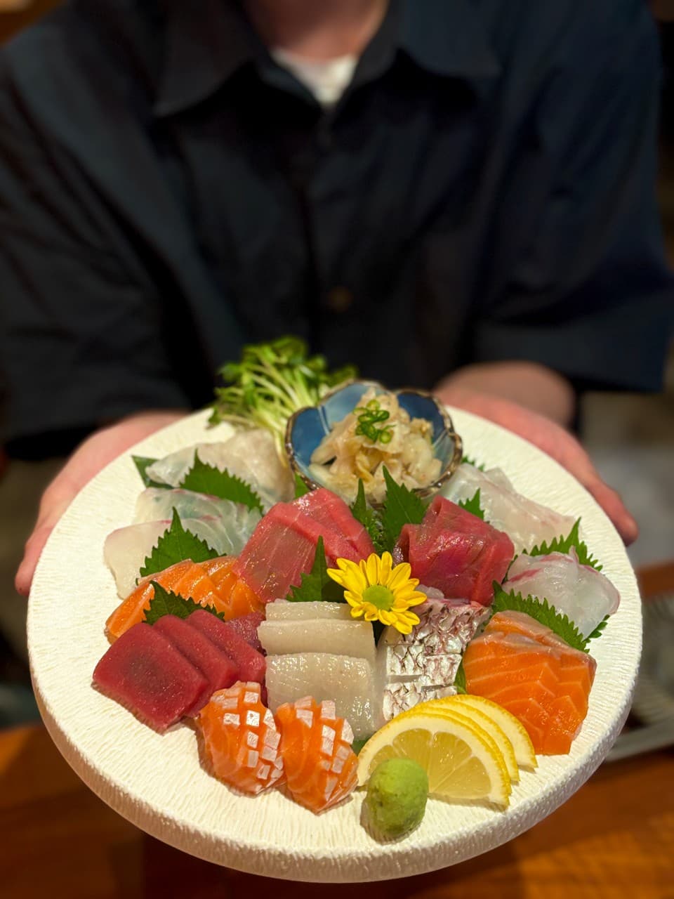 어두운 조명 아래 연어와 참치 등 다양한 생선회가 담긴 1인용 사시미 접시와 레몬, 고추냉이