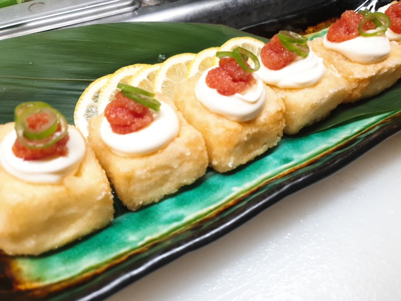 긴 접시 위 대나무 잎에 정렬된 명란 마요네즈 토핑의 두부 튀김과 곁들여진 레몬 슬라이스