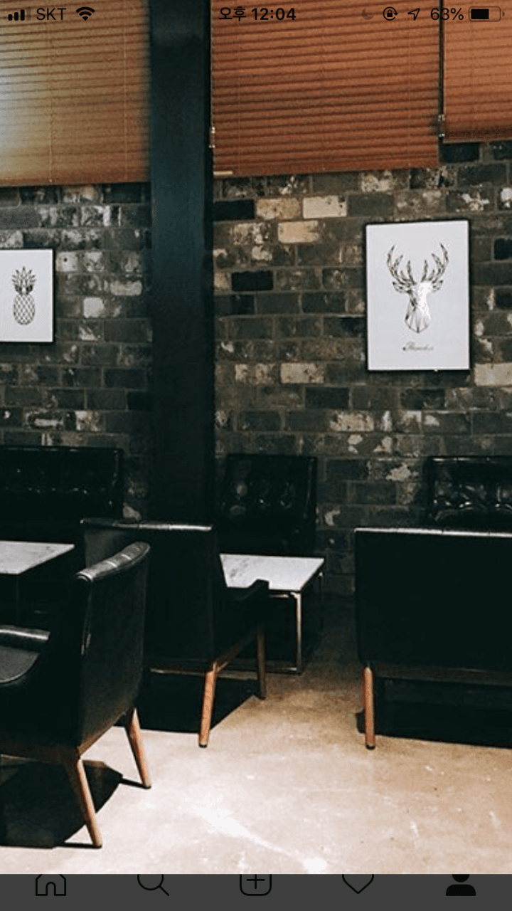 어두운 벽돌 벽을 배경으로 놓인 1인용 검은 가죽 의자와 대리석 테이블. 벽면의 사슴 액자와 창가의 나무 블라인드가 있는 내부 전경