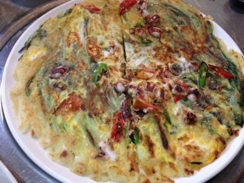 흰 접시에 담긴 오징어와 붉은 고추 고명의 노릇한 해물파전. 1인 좌석에서 술과 곁들이기 적당한 크기의 단품 요리