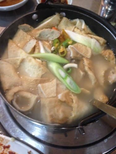 테이블 위 검은 전골 냄비에 담긴 다양한 모양의 어묵과 어긋썰기한 대파, 고추 고명이 올라간 1인용 어묵탕 전경