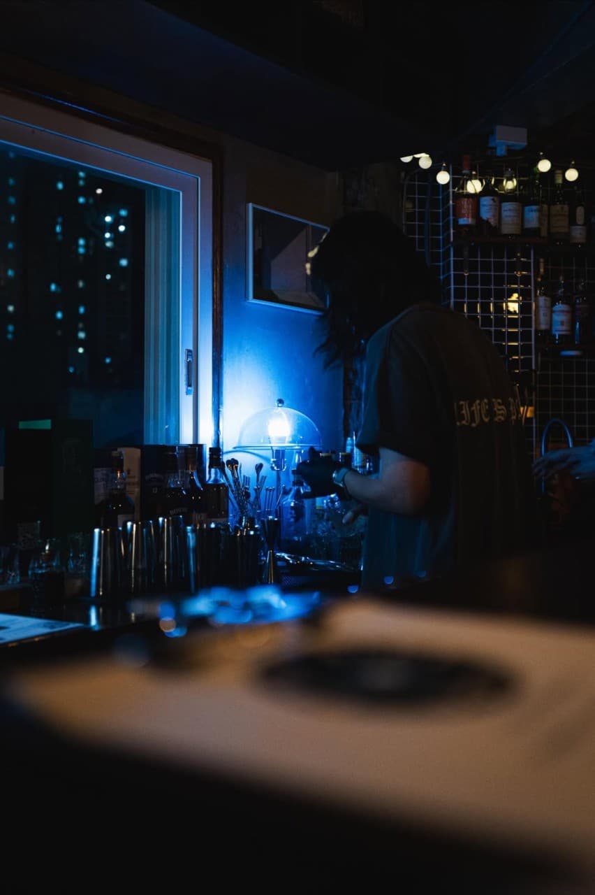 부산광역시 부산진구 페일블루닷 전포 바(Bar) 푸른 조명 아래 칵테일 쉐이커와 술병이 놓인 다찌석에서 바텐더가 음료를 제조하는 1인 혼술 공간