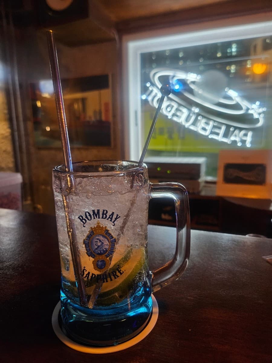 부산광역시 부산진구 페일블루닷 전포 바 다찌석에 놓인 봄베이 사파이어 하이볼. 얼음과 라임이 담긴 투명한 잔과 금속 빨대, 배경의 행성 네온 조명이 어우러진 혼술 상황