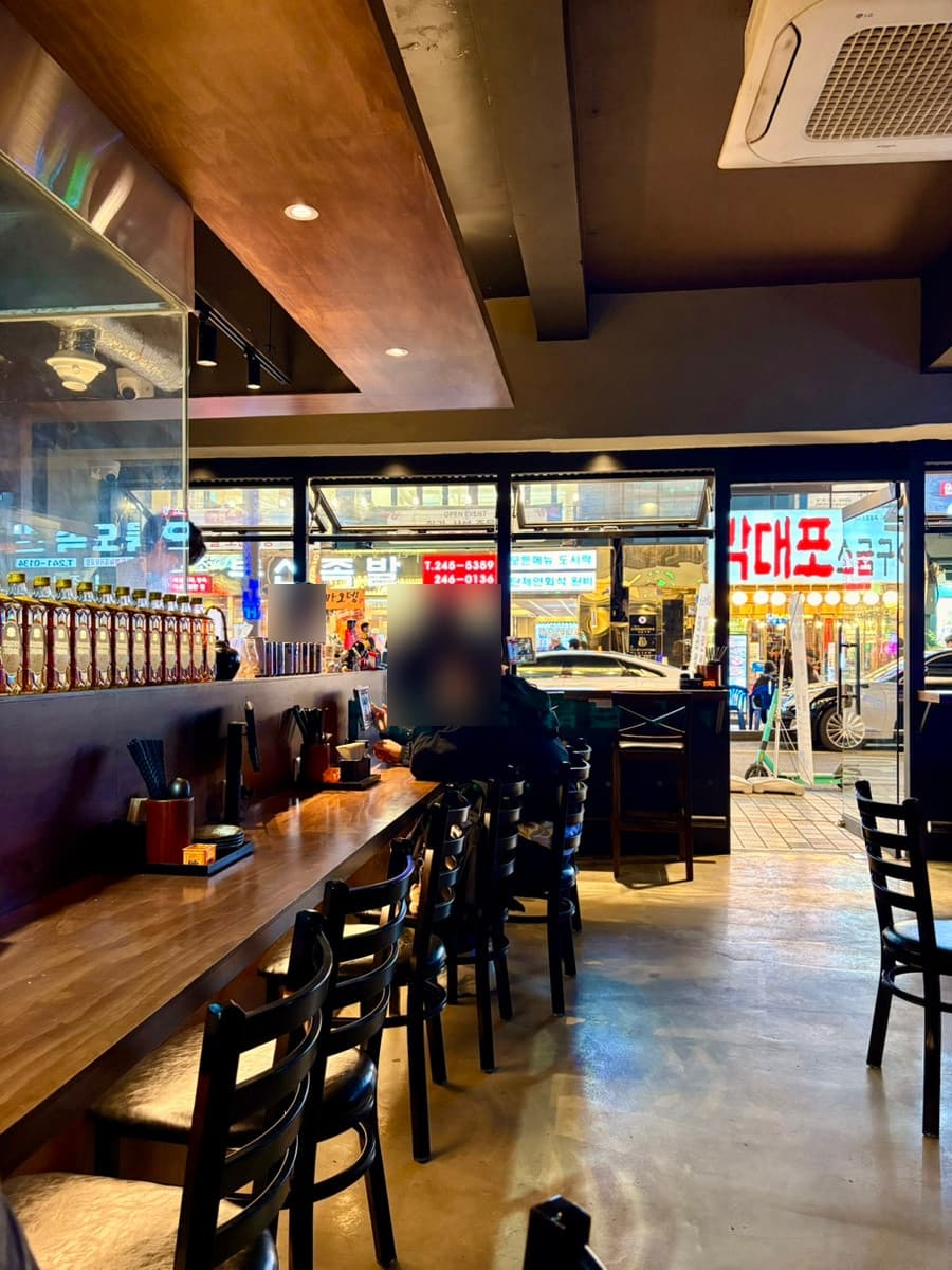 부산광역시 중구 요리주점 히노카오뎅 남포점 1인 다찌석 혼술. 낮은 조명 아래 목재 카운터와 진열된 위스키 병, 통유리 너머로 보이는 밤거리 풍경.