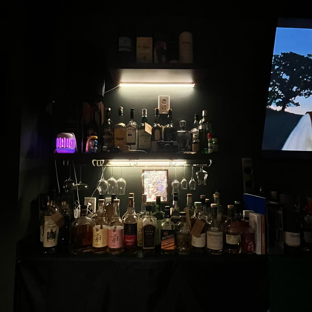 부산광역시 중구 맥주 호프 펍송 인 광복 - 은은한 조명 아래 정렬된 위스키 병들과 매달린 와인잔. 혼술 좌석 앞 다찌 선반에 놓인 다채로운 주류의 질감이 돋보임.